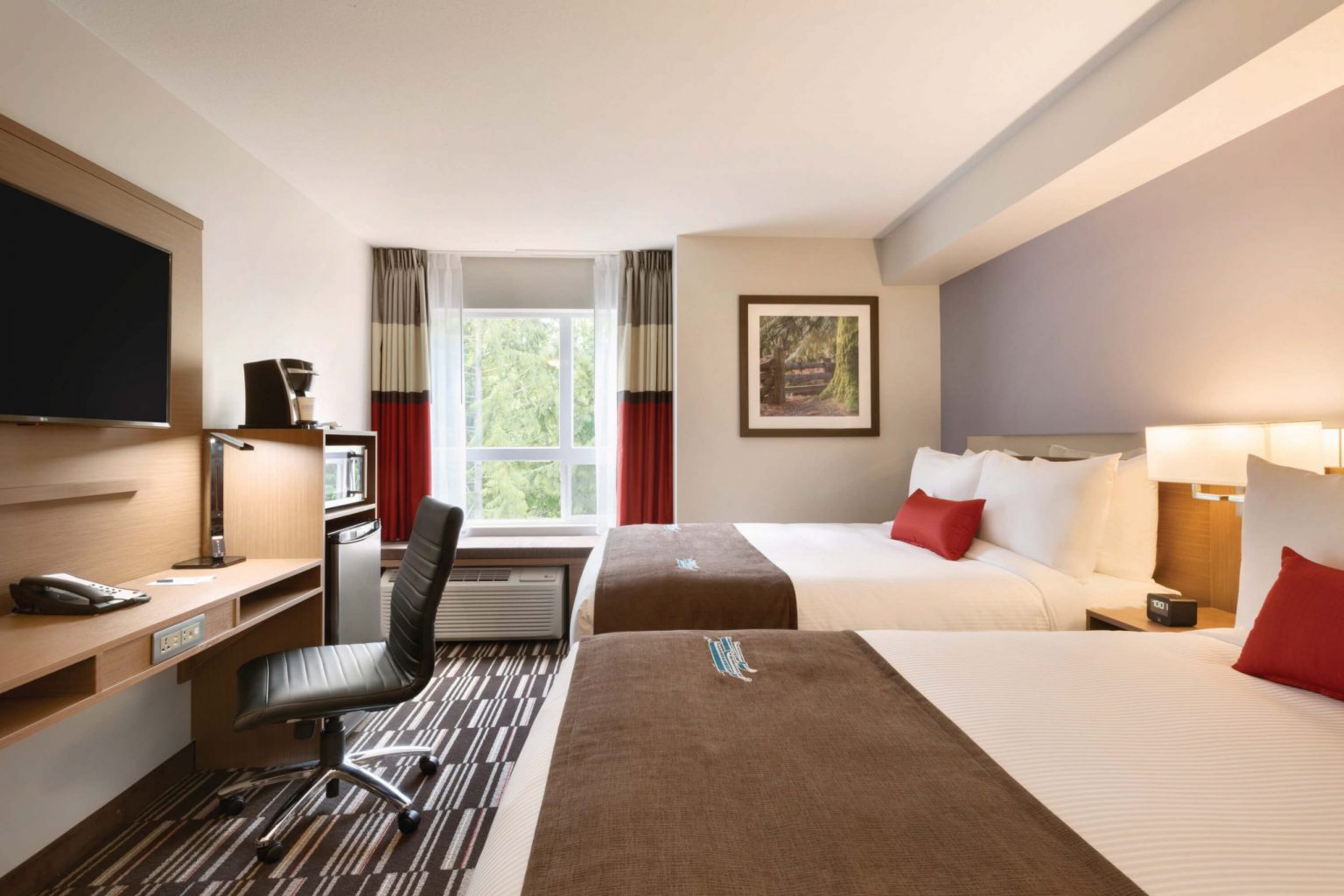 A hotel room with a bed, microwave, fridge, tv, and chair