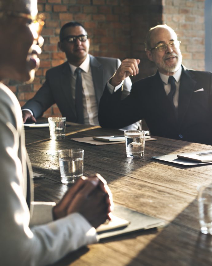 istockphoto-599491944-2048x2048 Businessmen sitting around a conference table watching a presentation