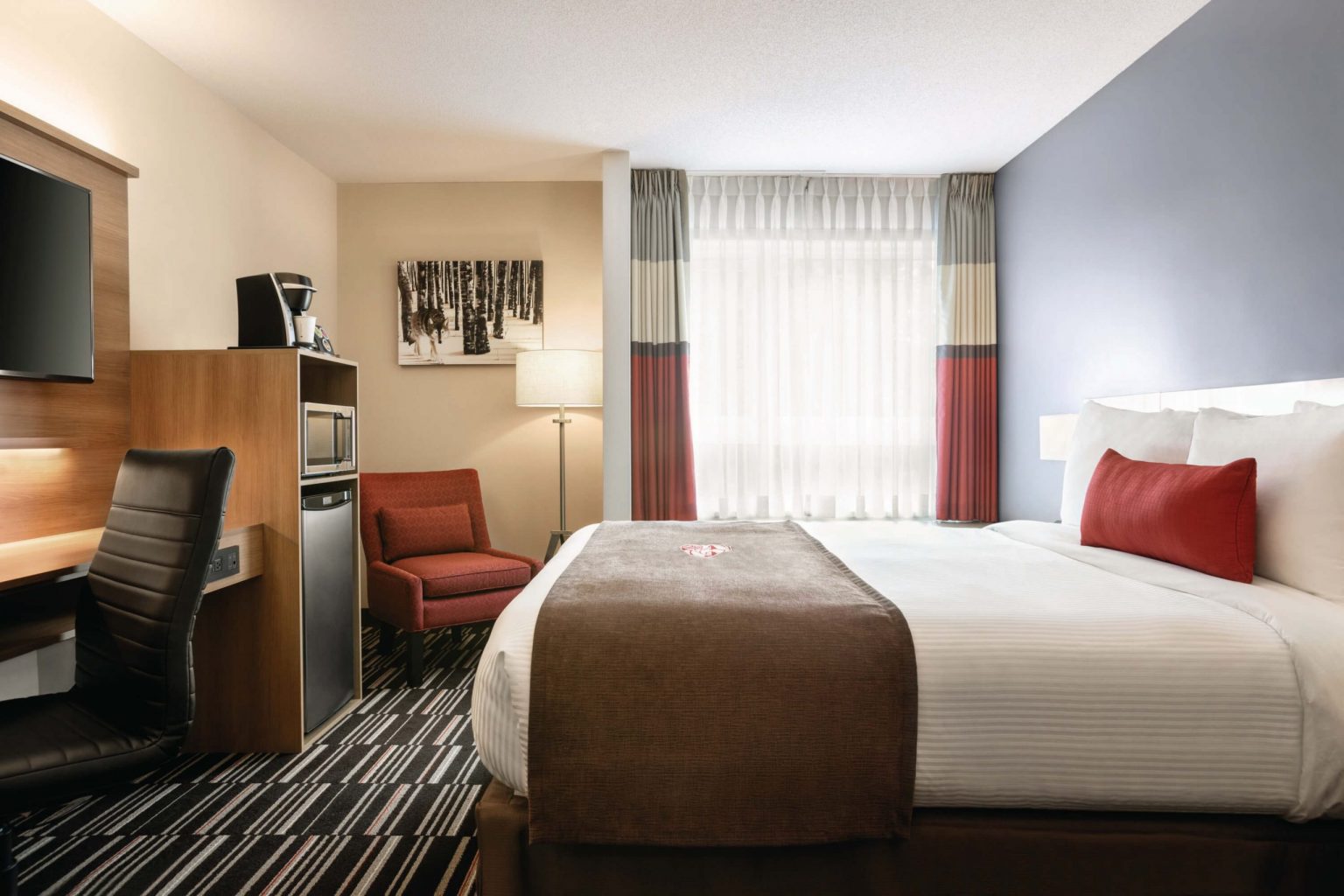 A hotel room with a bed, microwave, fridge, tv, and chairs